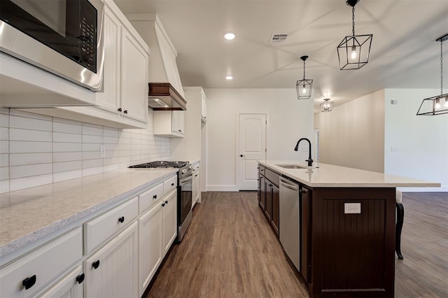 kitchen featuring sink, hanging light fixtures, stainless steel appliances, and an island with sink