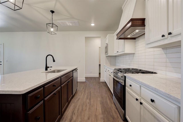 kitchen featuring a center island with sink, stainless steel appliances, decorative light fixtures, white cabinets, and sink