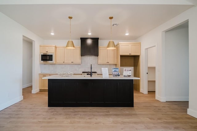 kitchen featuring pendant lighting, built in microwave, wall chimney range hood, and an island with sink