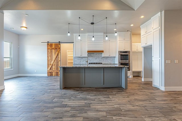 kitchen with stone counters, white cabinetry, a barn door, and a center island with sink