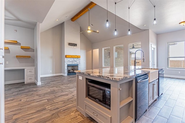 kitchen with a kitchen island with sink, dishwasher, built in microwave, hanging light fixtures, and light stone countertops