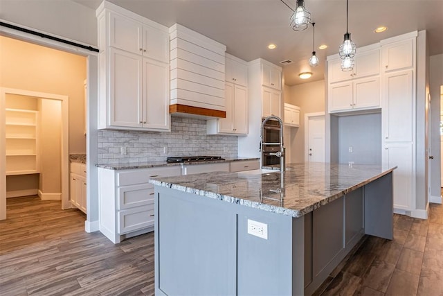 kitchen with decorative light fixtures, a spacious island, hardwood / wood-style floors, decorative backsplash, and white cabinetry