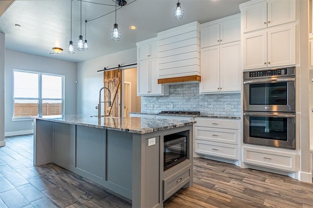 kitchen with white cabinets, a center island with sink, stainless steel appliances, and a barn door