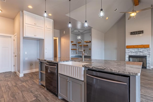 kitchen featuring pendant lighting, white cabinets, sink, light stone counters, and a center island with sink