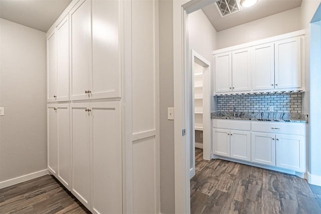 interior space with dark hardwood / wood-style floors, decorative backsplash, white cabinets, and light stone counters