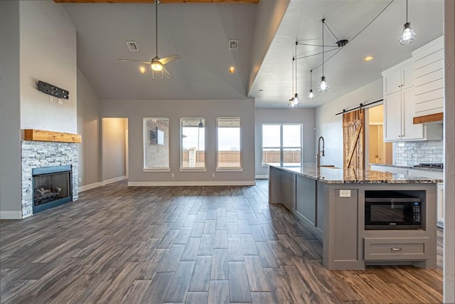 kitchen with white cabinets, black microwave, a stone fireplace, light stone counters, and a barn door