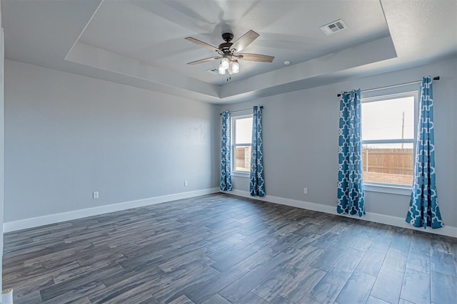 spare room with dark wood-type flooring, a tray ceiling, and ceiling fan