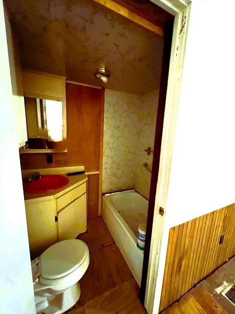 bathroom featuring toilet, vanity, wooden walls, and a washtub