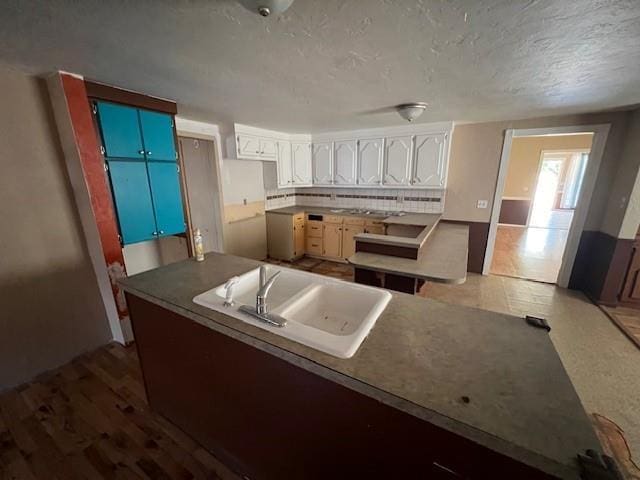 kitchen featuring kitchen peninsula, sink, decorative backsplash, and white cabinetry