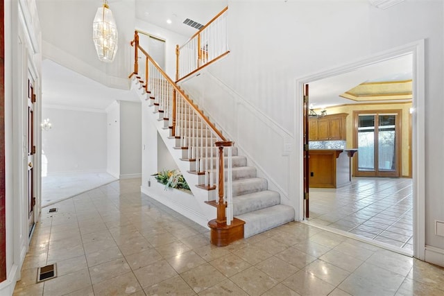 staircase featuring tile patterned floors, ornamental molding, a towering ceiling, and a notable chandelier