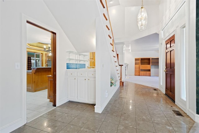 hallway with an inviting chandelier, light tile patterned flooring, and high vaulted ceiling