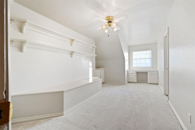 spacious closet with ceiling fan, lofted ceiling, built in desk, and light carpet