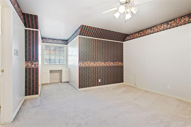 interior space featuring light carpet, built in desk, and ceiling fan