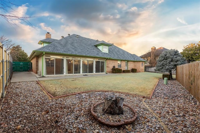 back house at dusk featuring a patio area and a lawn