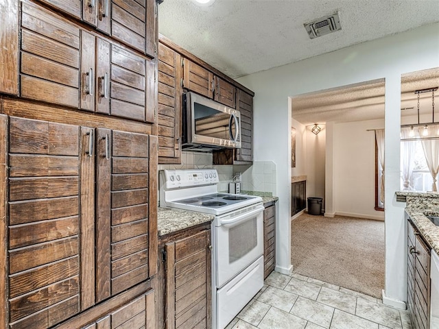 kitchen with visible vents, white range with electric cooktop, a textured ceiling, stainless steel microwave, and light carpet