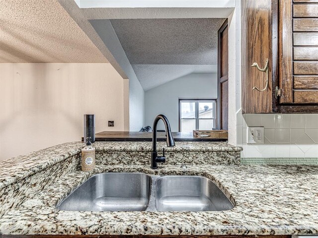 kitchen with light stone counters, a textured ceiling, tasteful backsplash, and a sink