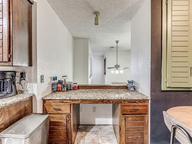 kitchen with a textured ceiling, built in study area, ceiling fan, and a textured wall