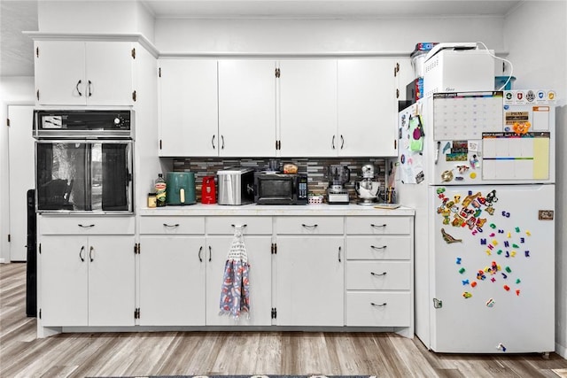 kitchen with black oven, decorative backsplash, light wood-type flooring, white refrigerator, and white cabinets