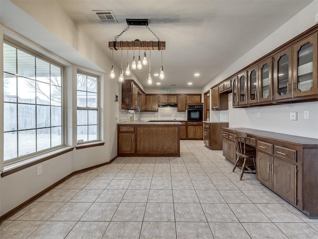 kitchen featuring light tile patterned floors, black oven, tasteful backsplash, decorative light fixtures, and built in desk