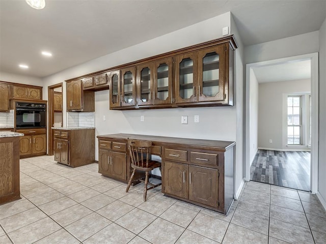 kitchen with tasteful backsplash, built in desk, light tile patterned flooring, dark brown cabinetry, and black oven