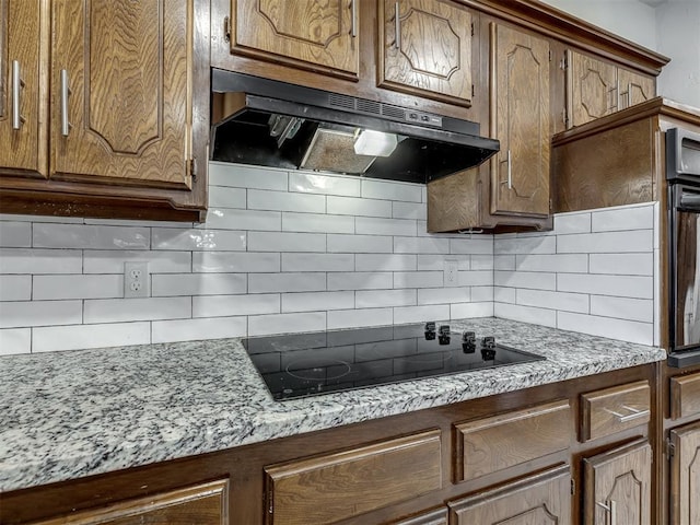 kitchen with light stone countertops, decorative backsplash, and black appliances