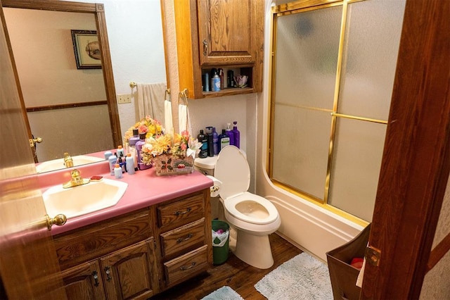 full bathroom with hardwood / wood-style floors, combined bath / shower with glass door, vanity, and toilet