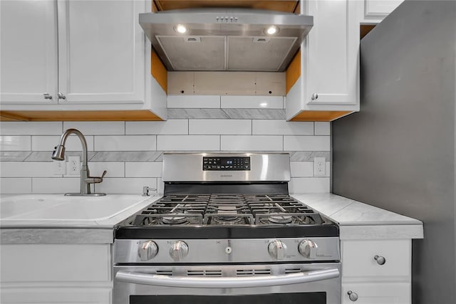 kitchen with tasteful backsplash, sink, stainless steel gas range, white cabinets, and light stone counters