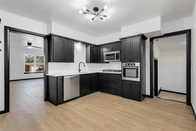 kitchen with appliances with stainless steel finishes, tasteful backsplash, light wood-type flooring, ceiling fan with notable chandelier, and sink