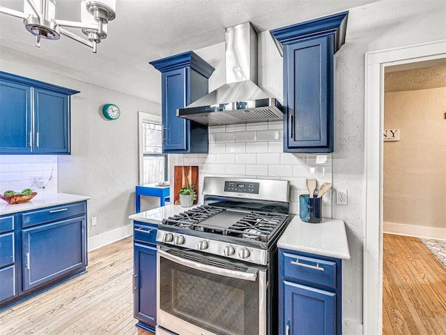 kitchen featuring tasteful backsplash, blue cabinets, stainless steel range with gas stovetop, and wall chimney exhaust hood