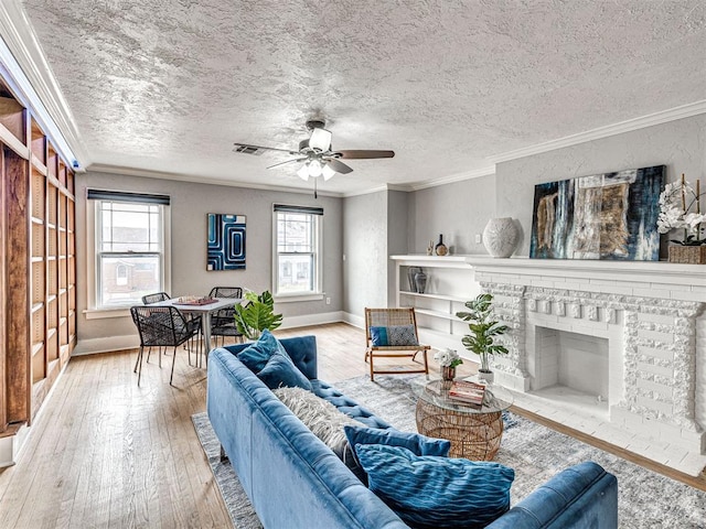 living room with crown molding, a textured ceiling, light wood-type flooring, ceiling fan, and a fireplace