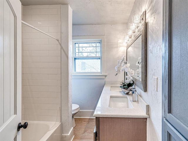 full bathroom with tiled shower / bath combo, vanity, a textured ceiling, and toilet