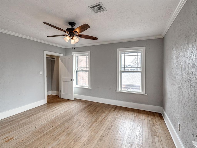 empty room featuring ceiling fan, ornamental molding, a textured ceiling, and light wood-type flooring