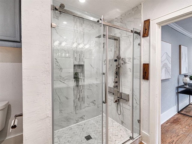 bathroom with hardwood / wood-style flooring, crown molding, a shower with door, and toilet