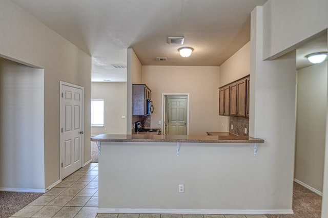 kitchen featuring light tile patterned floors, stove, backsplash, a kitchen bar, and kitchen peninsula