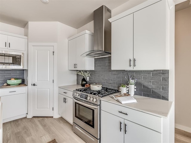 kitchen featuring white cabinetry, appliances with stainless steel finishes, decorative backsplash, and wall chimney range hood