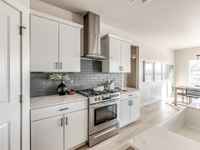 kitchen with white cabinetry, wall chimney exhaust hood, stainless steel gas range, and light stone counters