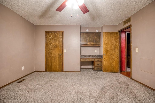 unfurnished bedroom featuring ceiling fan, a textured ceiling, built in desk, and carpet flooring