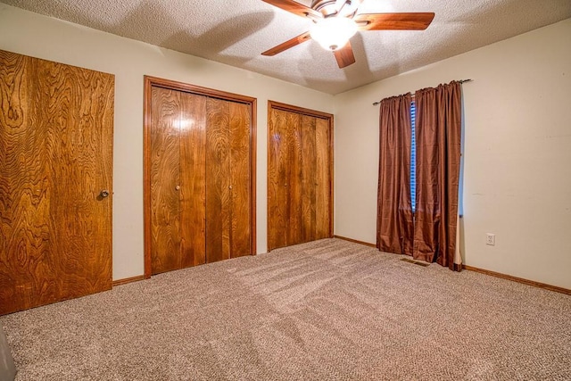 unfurnished bedroom with ceiling fan, a textured ceiling, carpet, and multiple closets