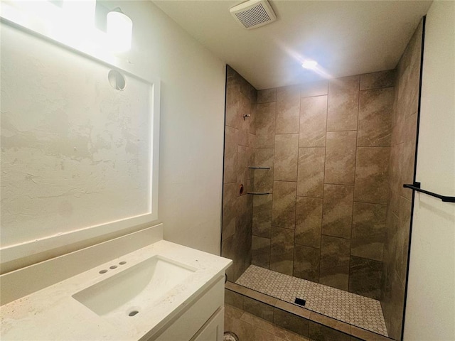 bathroom with visible vents, tiled shower, and vanity