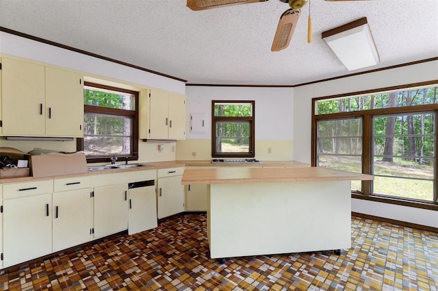 kitchen with sink, crown molding, a textured ceiling, a kitchen island, and ceiling fan