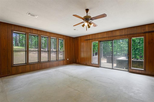 spare room with ceiling fan, a textured ceiling, and wood walls