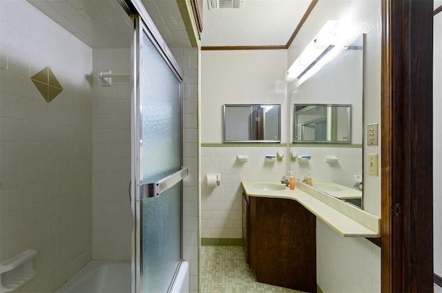 bathroom with crown molding, enclosed tub / shower combo, vanity, and tile walls