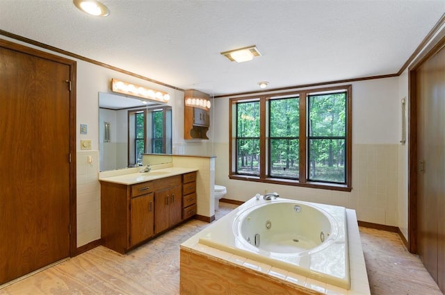 bathroom with toilet, a textured ceiling, tile walls, vanity, and tiled tub