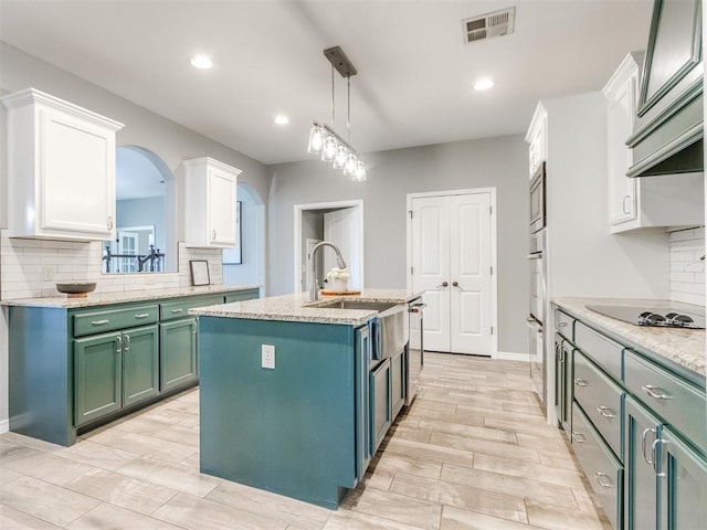 kitchen featuring appliances with stainless steel finishes, white cabinetry, sink, decorative light fixtures, and an island with sink