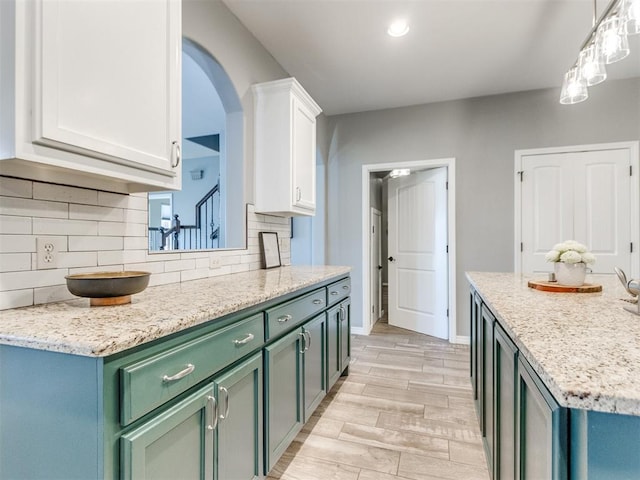 kitchen with light stone countertops, white cabinets, light hardwood / wood-style floors, decorative backsplash, and hanging light fixtures