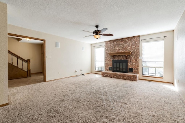 unfurnished living room with ceiling fan, light colored carpet, a textured ceiling, and a fireplace