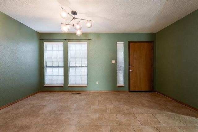 empty room with a textured ceiling and a chandelier