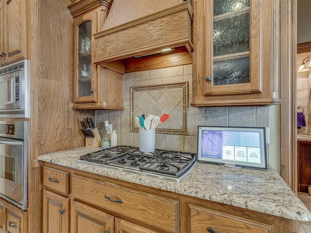 kitchen with premium range hood, stainless steel appliances, light stone countertops, and tasteful backsplash