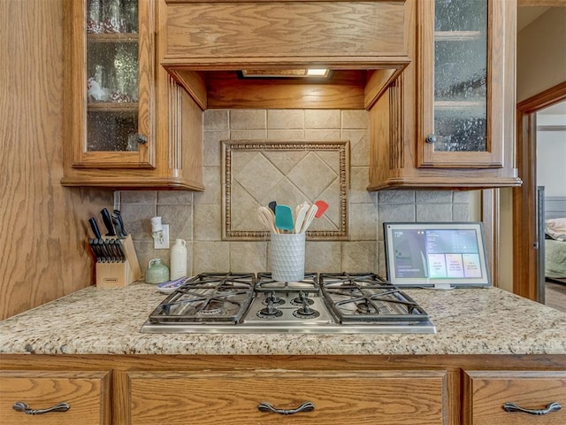 kitchen with tasteful backsplash, custom exhaust hood, light stone countertops, and stainless steel gas cooktop