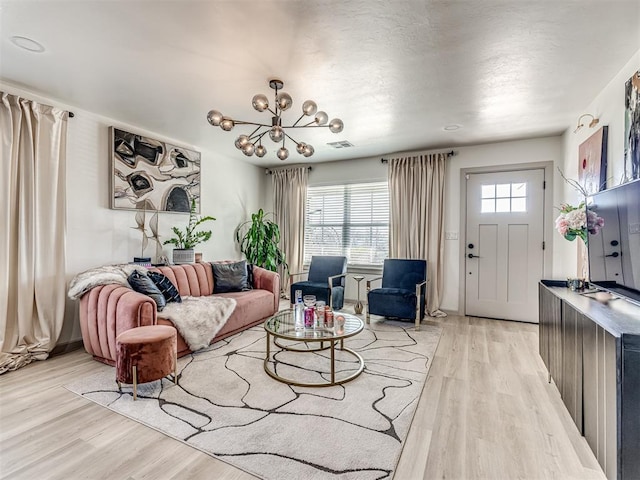 living room with a wealth of natural light, a notable chandelier, and light wood-type flooring